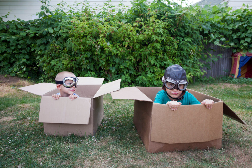 How much does a nanny cost in michigan Two brothers sit in boxes side by side in the backyard. They're both wearing aviator goggles, and older brother has a leather cap to match. They're in a heated race, with younger brother slightly behind. Who will win?